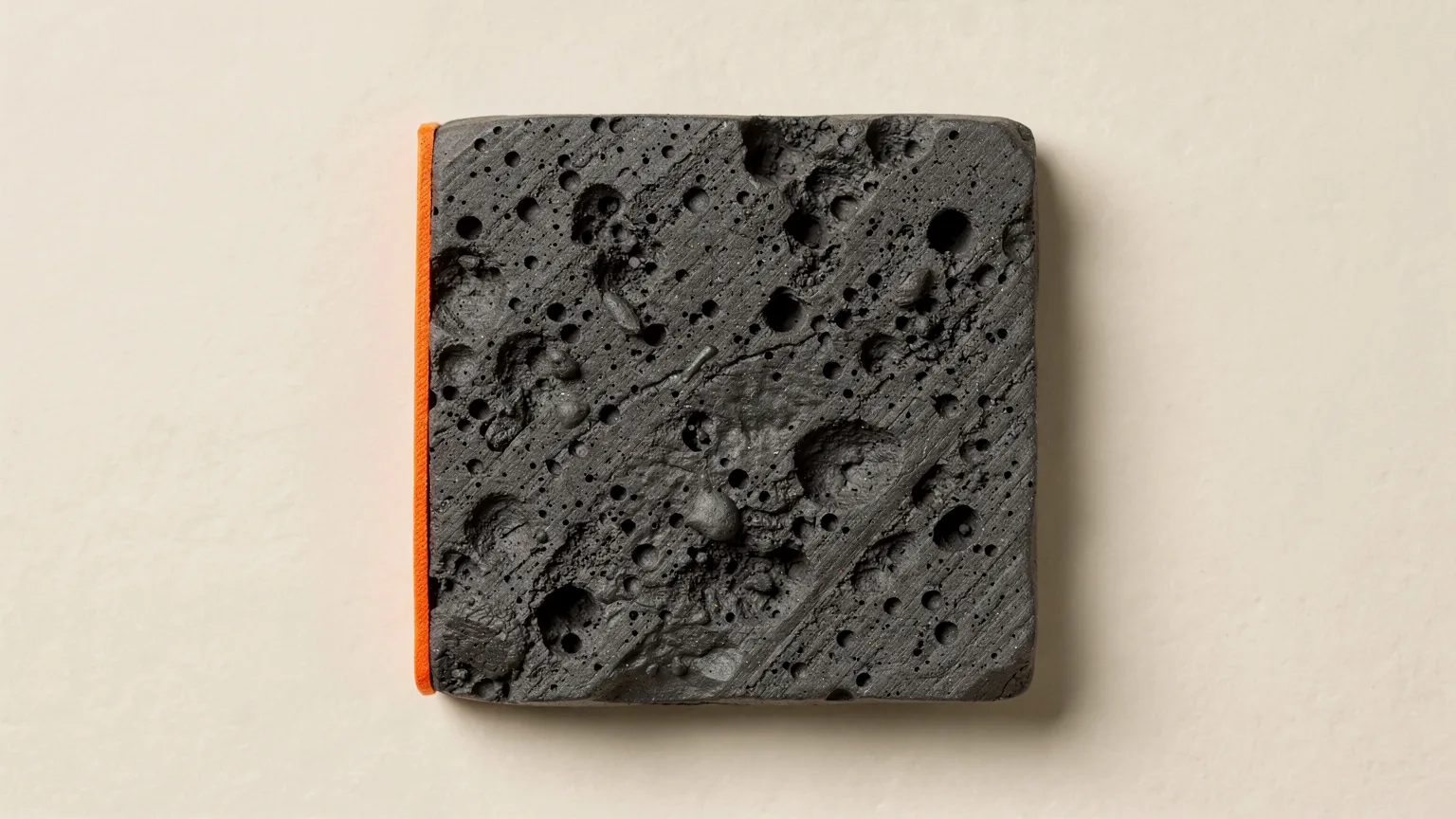 Illustration: a top-down close-up of a graphite printed square top surface with visible gaps and soft pillowed dips, one orange line along an edge