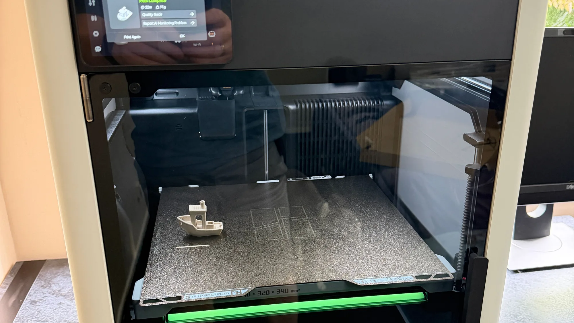 An enclosed 3D printer with its glass door open showing the print bed and a small print
