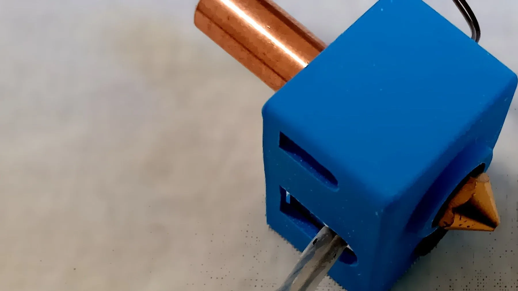 A 3D printer hotend with a copper heat break and a brass nozzle in a blue silicone cover