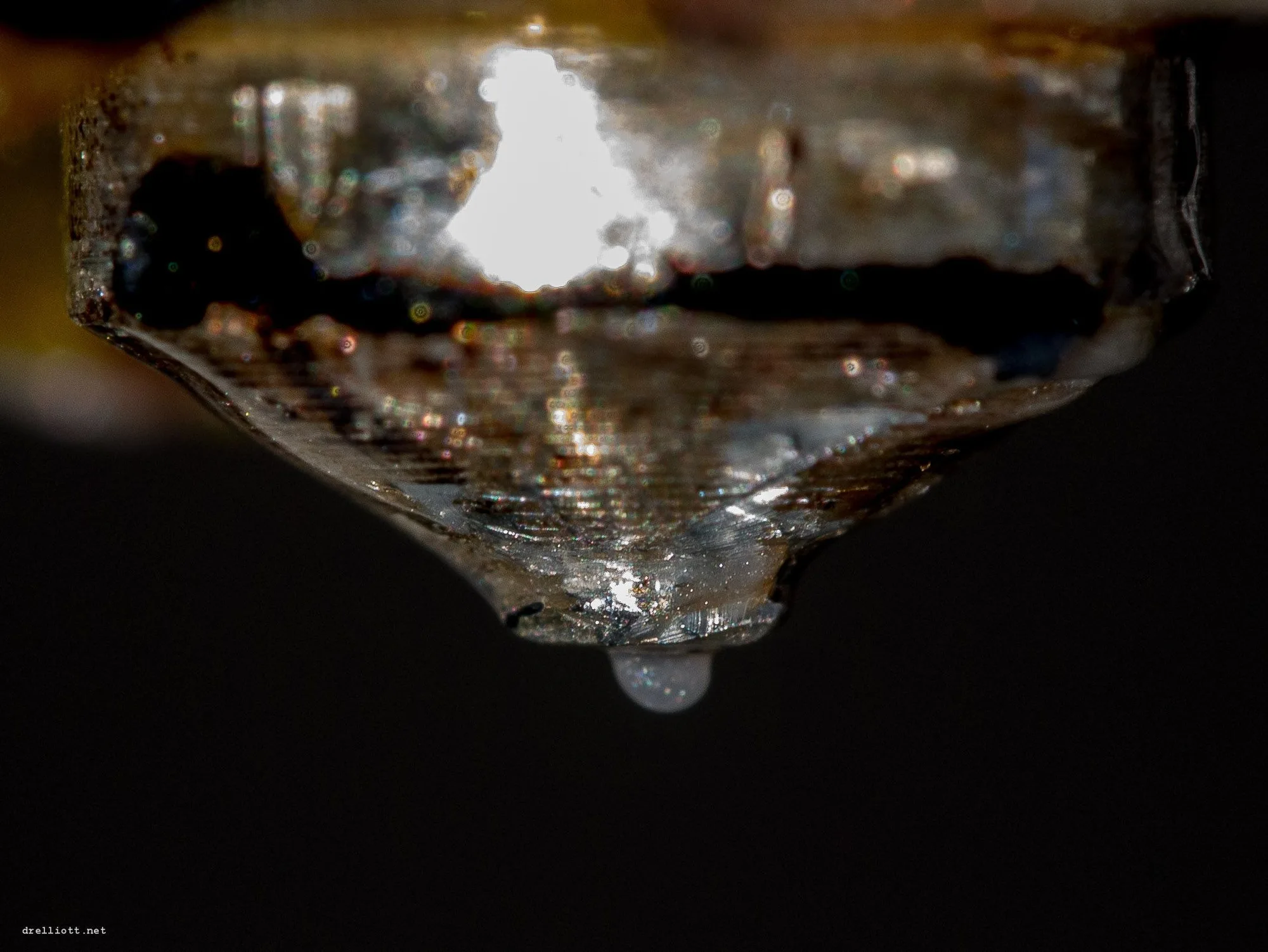 Close-up of a 3D printer nozzle with a bead of molten plastic hanging from the tip