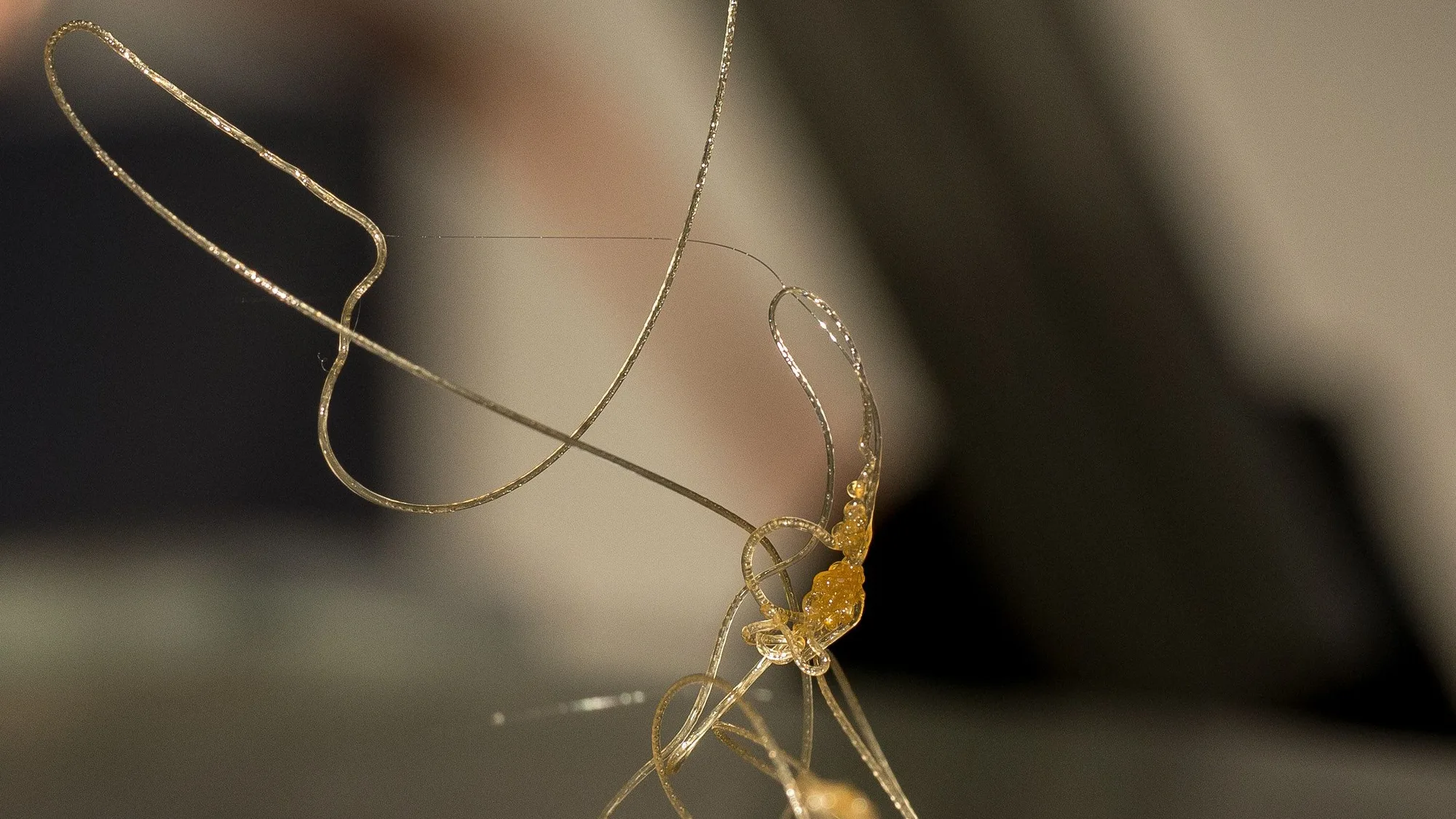 Close-up of a 3D printer nozzle with fine strands of plastic trailing from it